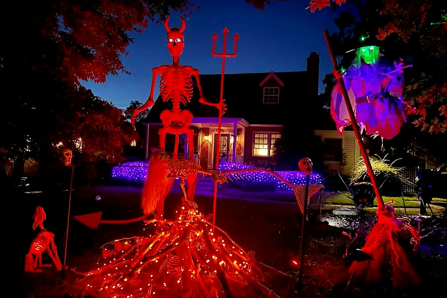 Giant skeleton, witch and lit pathway in front of a cottage at dusk