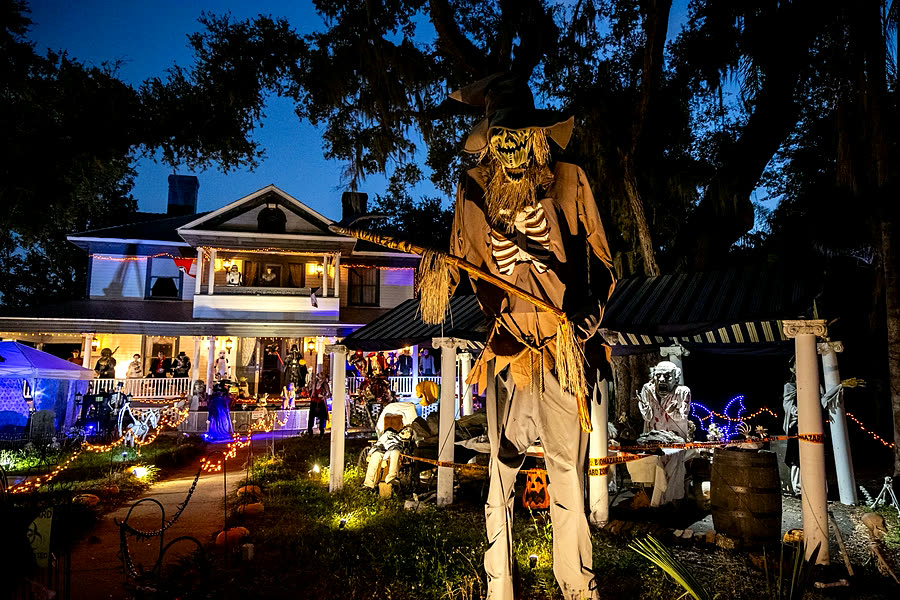 Home glowing with Halloween lights and a giant scarecrow at dusk