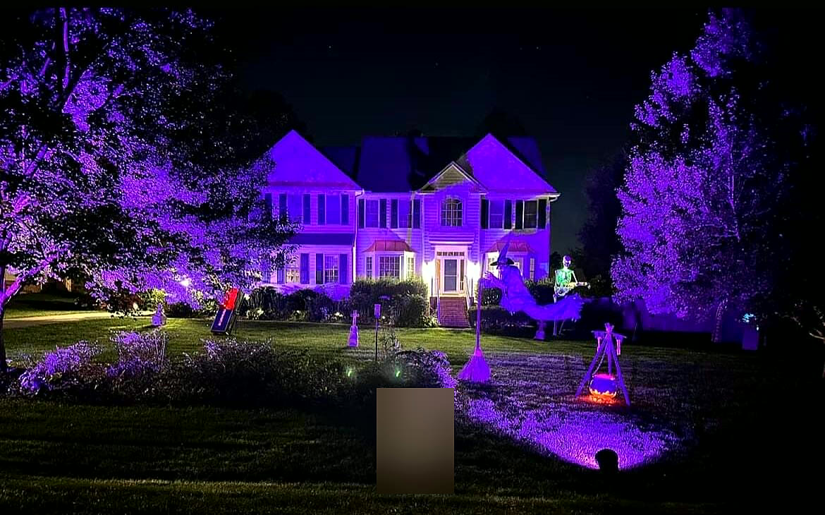 Colonial home washed in purple uplighting with a flying witch
