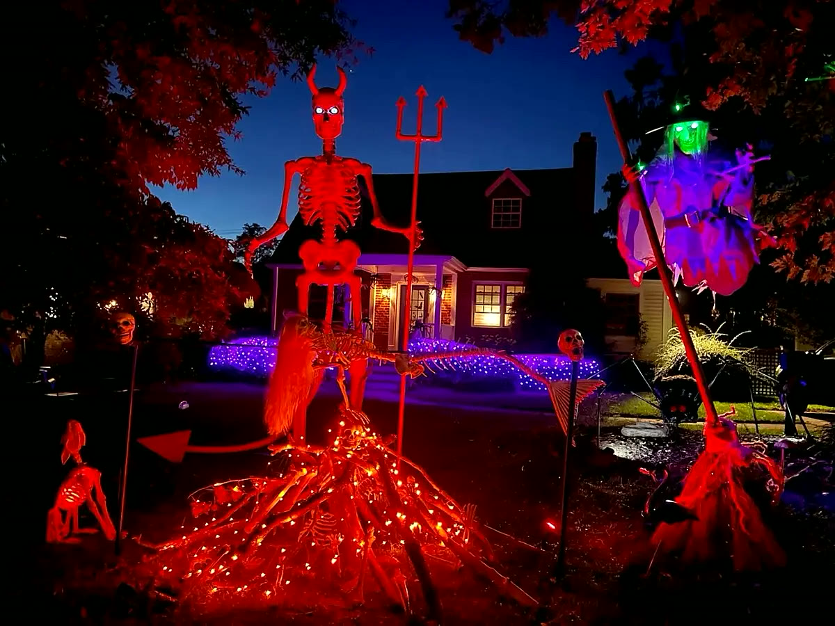 Cottage at dusk with a giant red devil skeleton, a witch and lit pathway